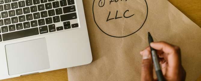 Laptop and scrap paper someone wrote 1 Form LLC on. A hand with a pen